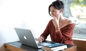 Kobieta zamyślona nad ekranem laptopa, przygotowująca udostępnianie ekranu podczas wideokonferencji.