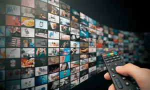 Dłoń trzyma pilota, wybierając treści z zakrzywionego ekranu pełnego miniatur, jak w interaktywnym menu HbbTV.