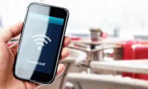 Dłoń trzyma smartfon z napisem "Connected" i ikoną Wi-Fi. W tle widać stoliki kawiarniane.