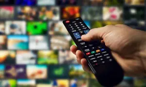 Dłoń trzyma pilot, gotowa do nauki, jak programować pilot do telewizora, przeglądając menu na ekranie.