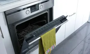 Otwarty piekarnik z zielonym ręcznikiem na drzwiczkach. W środku kratka i naczynie. Piekarnik ma funkcję pyrolizy.