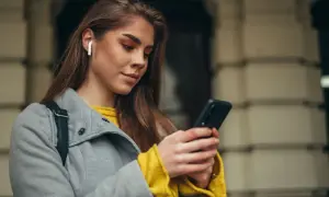 Kobieta w białych słuchawkach bezprzewodowych korzysta z telefonu, ucząc się, jak sparować słuchawki z telefonem.