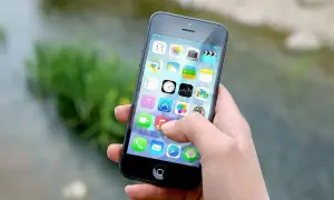 Dłoń trzyma iPhone'a z widocznymi ikonami aplikacji. Zastanawiasz się, jak wyłączyć iPhone'a?