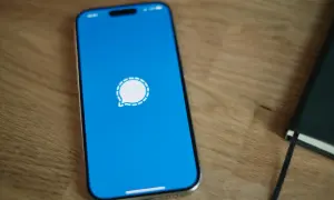 Telefon z niebieskim ekranem i ikoną komunikatora Signal. Obok leży czarny notatnik.