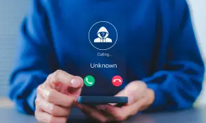 Osoba trzyma telefon, na ekranie którego widnieje przychodzące połączenie od nieznanego numeru. To dobry moment, by dowiedzieć się, jak zablokować numer.