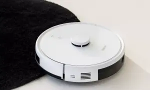 Biały robot sprzątający obok czarnego dywanika. Jego moc ssania odkurzacza poradzi sobie z każdym brudem.