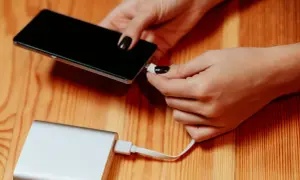 Dłonie podłączają telefon do powerbanku, by naładować baterię. Duża pojemność mah zapewni długie działanie.