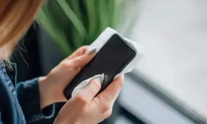 Dłonie z paznokciami w szarym lakierze wykonują czyszczenie telefonu chusteczką.