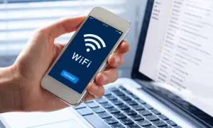 Dłoń trzyma smartfon z ikoną WiFi i napisem "Connect". Obok leży laptop z widokiem skrzynki mailowej. Dostęp do sieci, być może przez **ssid**, jest kluczowy.