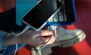Dłoń podłącza kabel USB, tworząc łącze z telefonem leżącym na niebieskim laptopie.