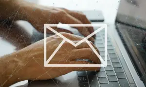 Dłonie piszą na klawiaturze laptopa, nad nimi biała ikona koperty i sieć połączeń. Uważaj na spam!