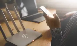 Router z czerwoną diodą i ręka trzymająca telefon. Brak internetu uniemożliwia pracę na laptopie.