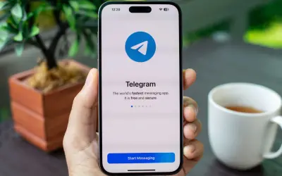 Dłoń trzyma smartfon z ekranem startowym aplikacji Telegram. To szybka, darmowa i bezpieczna aplikacja do wysyłania wiadomości.