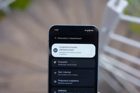 Ekran telefonu z powiadomieniem o aktualizacji systemu. Widoczna jest godzina 11:29, ikona 5G, poziom baterii 64% i menu ustawień, w tym opcje "Sieć i internet" oraz "Połączone urządzenia", typowe dla systemu Android 16.