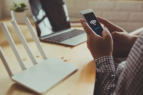 Dłoń trzyma smartfon z ikoną Wi-Fi i przyciskiem "connect", obok router i laptop. Szybkie połączenie dzięki wifi direct.