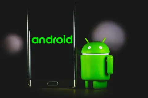 Zielony robot Android obok telefonu z napisem "android 13" na ekranie.