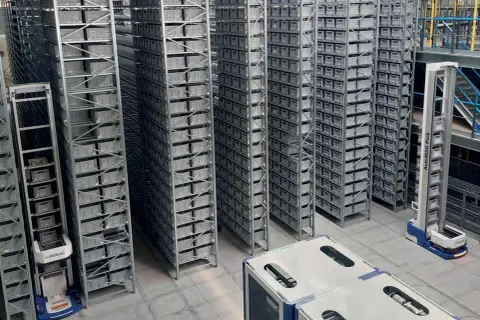 Automatyczny system magazynowy z regałami pełnymi pojemników, zrobotyzowane wózki poruszają się po hali. Wózki te, odporne na warunki **IP67**, zapewniają efektywne zarządzanie zapasami.