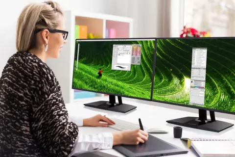 Kobieta pracuje przy dwóch monitorach z wąską ramką (bezel), edytując zdjęcie tarasów ryżowych.