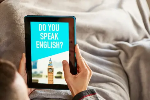 Osoba korzysta z aplikacji do nauki angielskiego na tablecie. Na ekranie widnieje pytanie "DO YOU SPEAK ENGLISH?" i miniatura Big Bena.