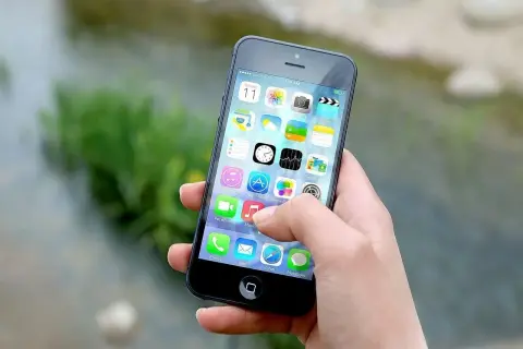 Dłoń trzyma iPhone'a z widocznymi ikonami aplikacji. Zastanawiasz się, jak wyłączyć iPhone'a?