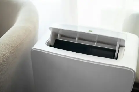 Nowoczesny klimatyzator bez jednostki zewnętrznej, z otwartą klapą wentylacyjną, obok jasnej kanapy.