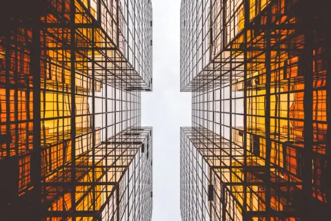 Szklane wieżowce odbijające pomarańczowe światło, tworzące geometryczny wzór. Czysta architektura w nowoczesnym wydaniu.