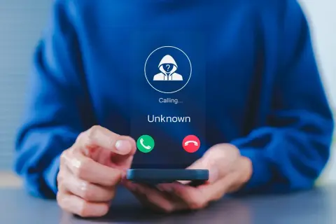 Osoba trzyma telefon, na ekranie którego widnieje przychodzące połączenie od nieznanego numeru. To dobry moment, by dowiedzieć się, jak zablokować numer.