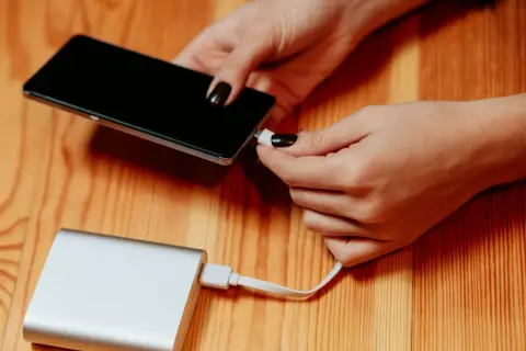 Dłonie podłączają telefon do powerbanku, by naładować baterię. Duża pojemność mah zapewni długie działanie.