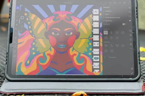 Kolorowy portret kobiety z motylimi skrzydłami, tworzony w aplikacji Adobe Fresco na tablecie. Widoczne narzędzia symetrii.