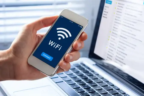Dłoń trzyma smartfon z ikoną WiFi i napisem "Connect". Obok leży laptop z widokiem skrzynki mailowej. Dostęp do sieci, być może przez **ssid**, jest kluczowy.
