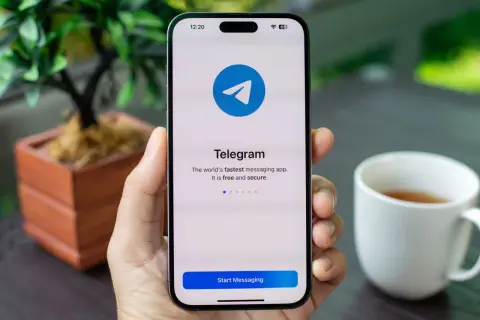 Dłoń trzyma smartfon z ekranem startowym aplikacji Telegram. To szybka, darmowa i bezpieczna aplikacja do wysyłania wiadomości.