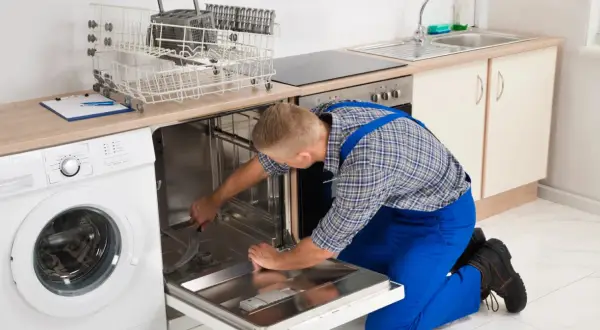Serwisant naprawia zmywarkę Bosch, która wyświetla błąd E15. Widać też pralkę i kosze na naczynia.