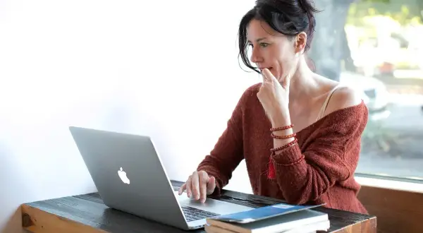 Kobieta zamyślona nad ekranem laptopa, przygotowująca udostępnianie ekranu podczas wideokonferencji.