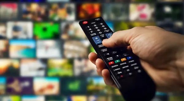 Dłoń trzyma pilot, gotowa do nauki, jak programować pilot do telewizora, przeglądając menu na ekranie.