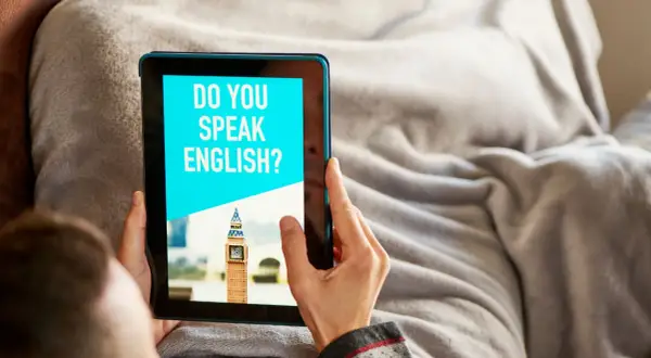 Osoba korzysta z aplikacji do nauki angielskiego na tablecie. Na ekranie widnieje pytanie "DO YOU SPEAK ENGLISH?" i miniatura Big Bena.