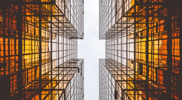 Szklane wieżowce odbijające pomarańczowe światło, tworzące geometryczny wzór. Czysta architektura w nowoczesnym wydaniu.