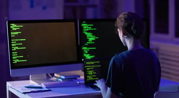 Kobieta programistka pracuje nocą nad kodem. Na ekranach widać zielony tekst, a w pomieszczeniu panuje niebiesko-fioletowe oświetlenie. To jej codzienny crud.