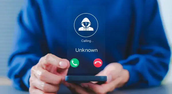 Osoba trzyma telefon, na ekranie którego widnieje przychodzące połączenie od nieznanego numeru. To dobry moment, by dowiedzieć się, jak zablokować numer.