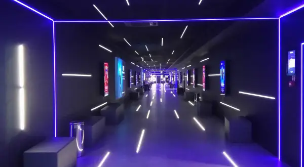Nowoczesny korytarz multikina z neonowym oświetleniem, idealny do projekcji filmowych dzięki zaawansowanemu projektorowi laserowemu.