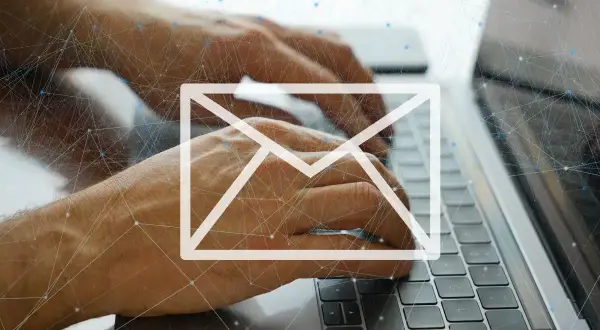 Dłonie piszą na klawiaturze laptopa, nad nimi biała ikona koperty i sieć połączeń. Uważaj na spam!
