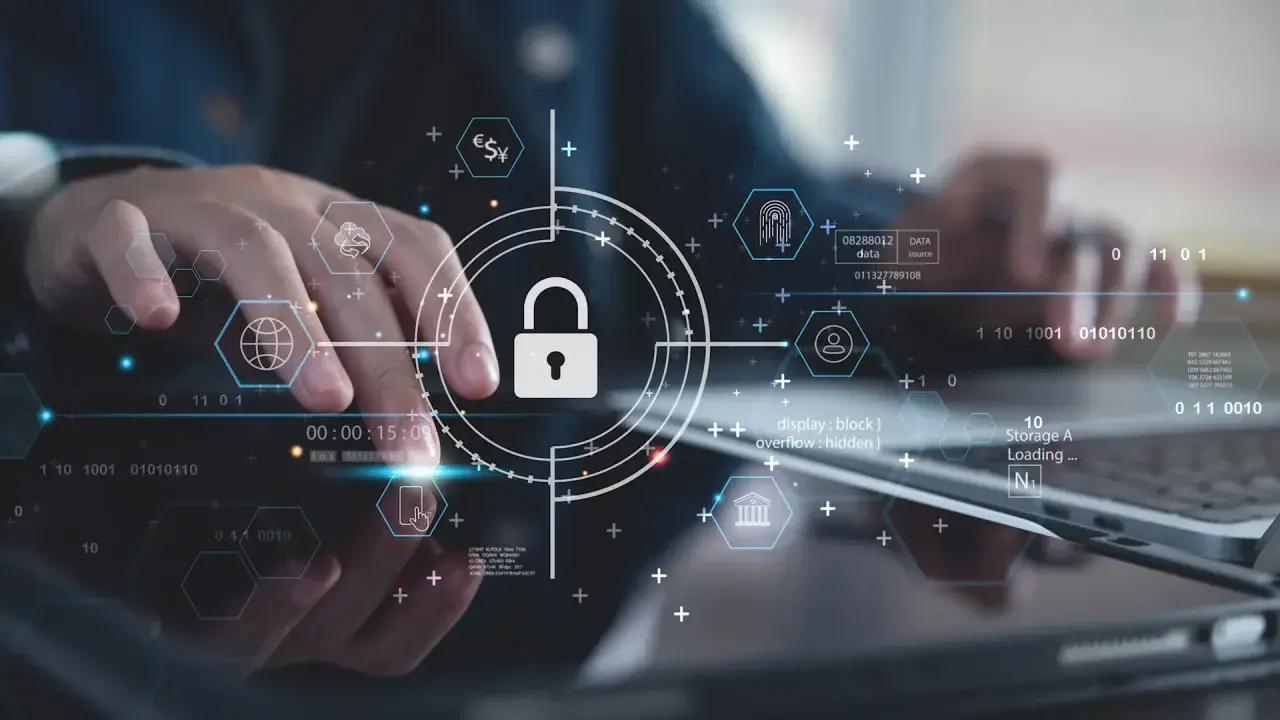 Ręce pracujące nad technologią, symbol kłódki i ikony sieciowe podkreślają znaczenie cyber security.