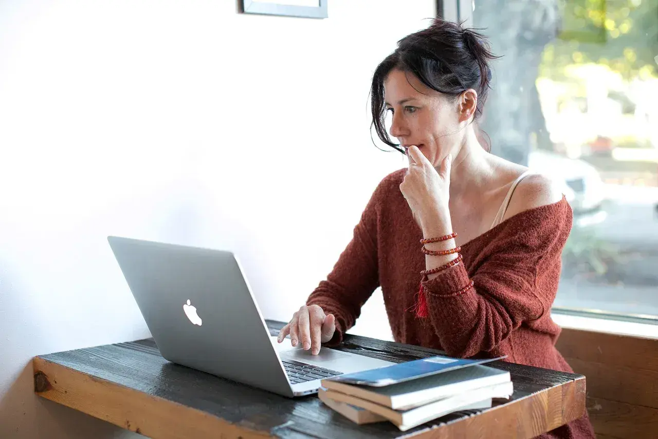 Kobieta zamyślona nad ekranem laptopa, przygotowująca udostępnianie ekranu podczas wideokonferencji.