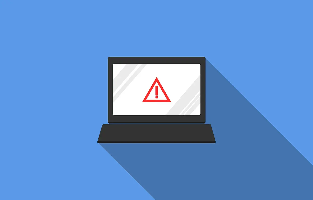Laptop z czerwonym znakiem ostrzegawczym na ekranie. Symbolizuje zagrożenie w cyberbezpieczeństwie.