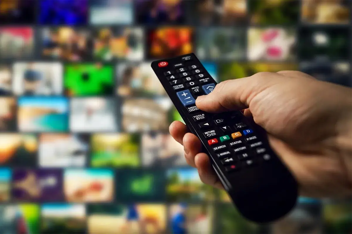 Dłoń trzyma pilot, gotowa do nauki, jak programować pilot do telewizora, przeglądając menu na ekranie.