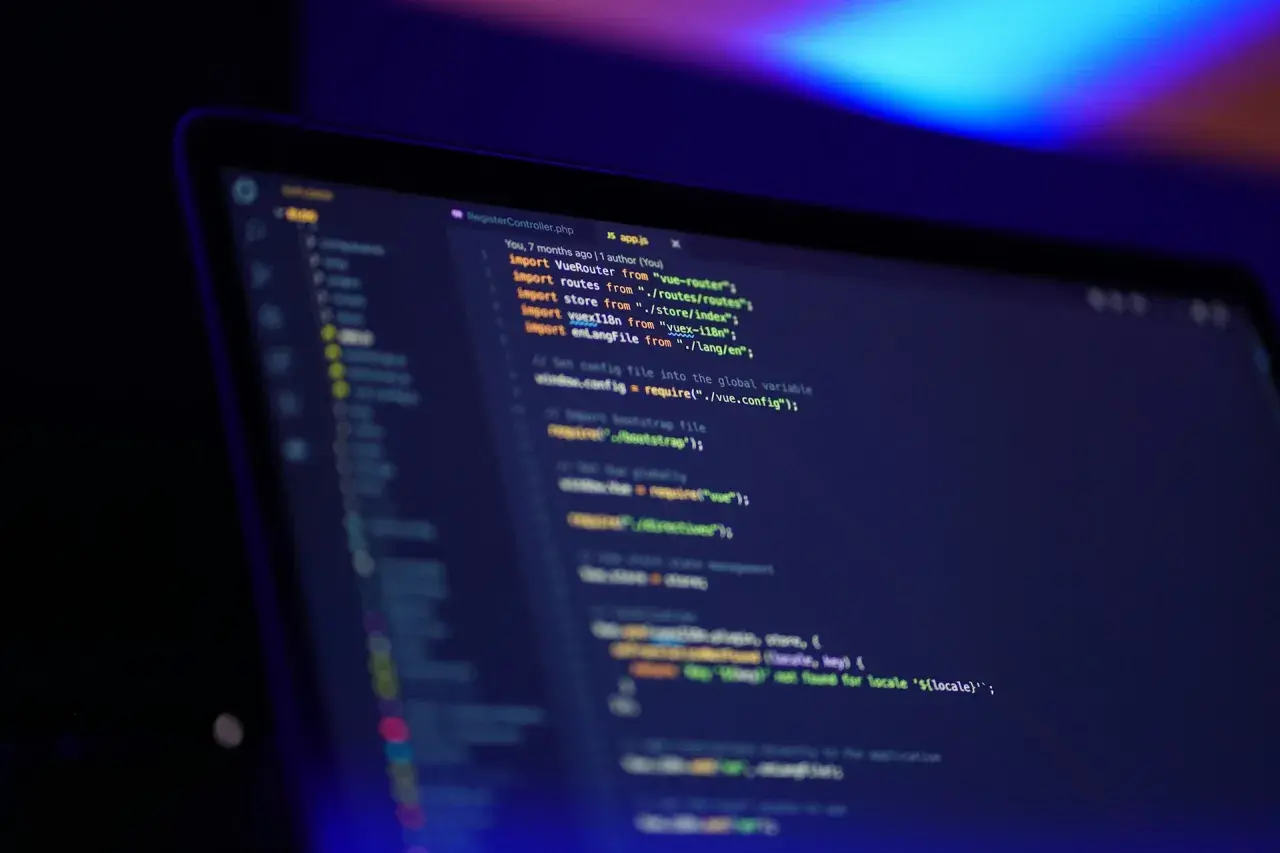 Kod JavaScript na ekranie laptopa, widać fragmenty kodu, importy i komentarze. Oop!