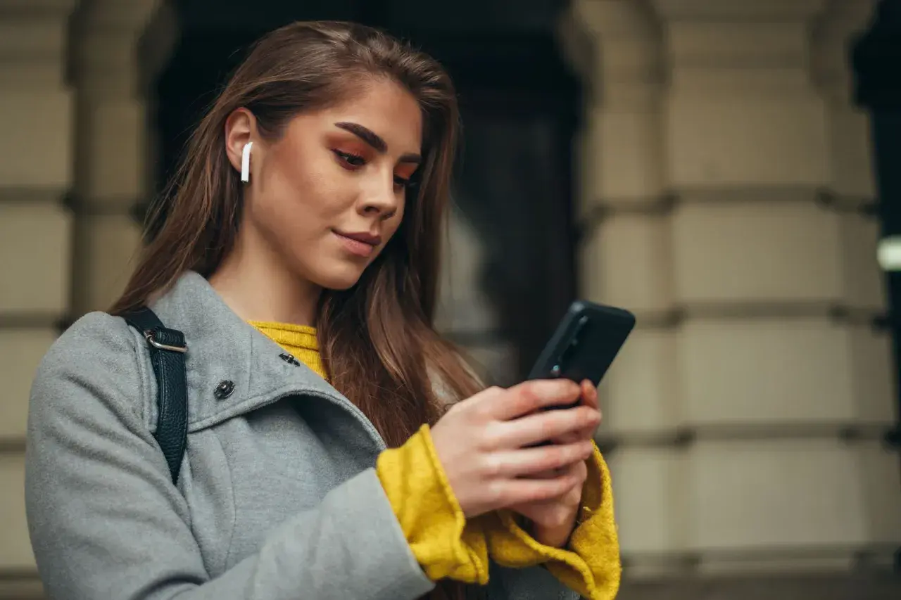 Kobieta w białych słuchawkach bezprzewodowych korzysta z telefonu, ucząc się, jak sparować słuchawki z telefonem.