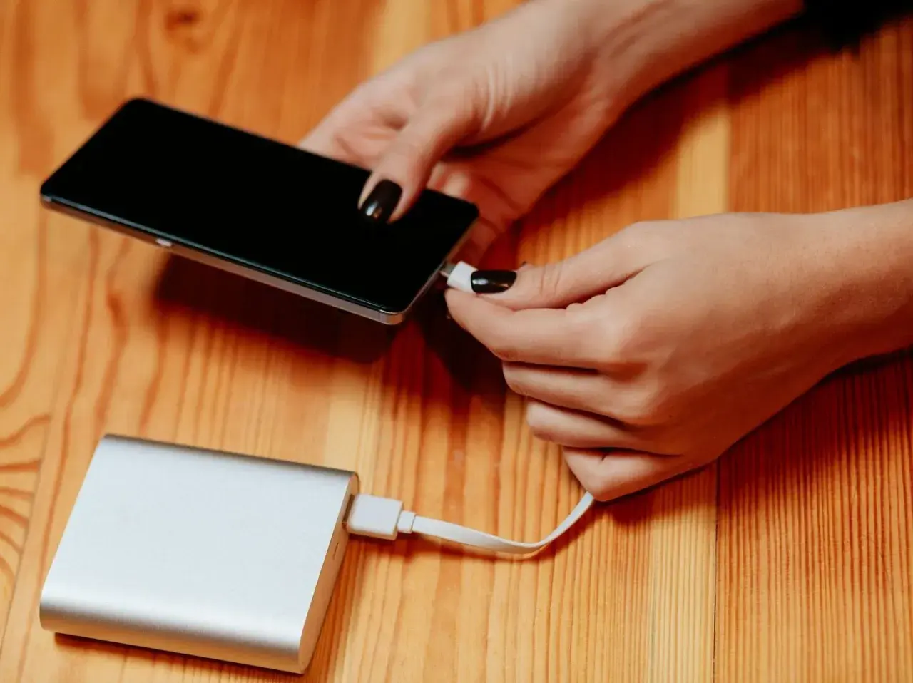 Dłonie podłączają telefon do powerbanku, by naładować baterię. Duża pojemność mah zapewni długie działanie.