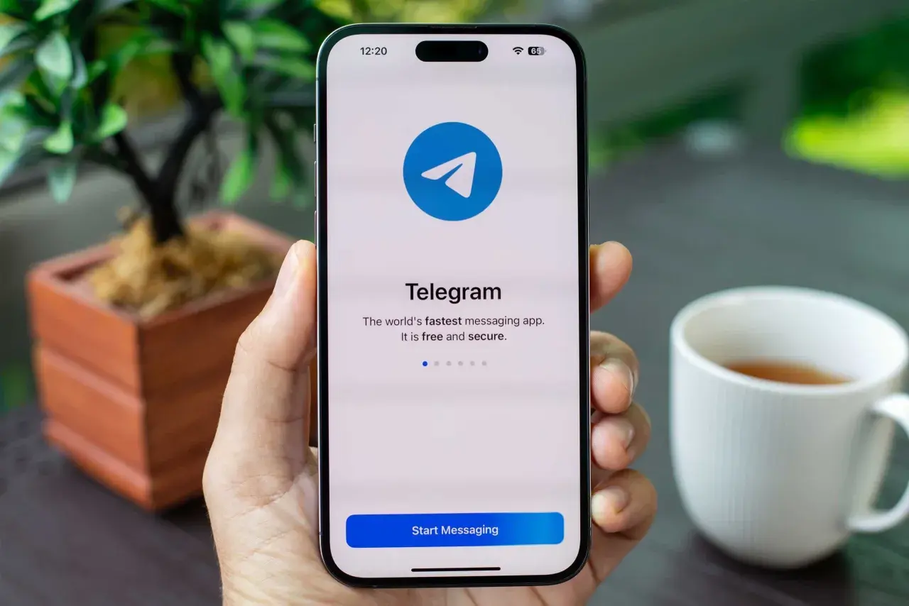Dłoń trzyma smartfon z ekranem startowym aplikacji Telegram. To szybka, darmowa i bezpieczna aplikacja do wysyłania wiadomości.