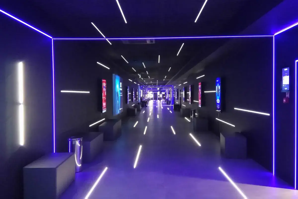 Nowoczesny korytarz multikina z neonowym oświetleniem, idealny do projekcji filmowych dzięki zaawansowanemu projektorowi laserowemu.