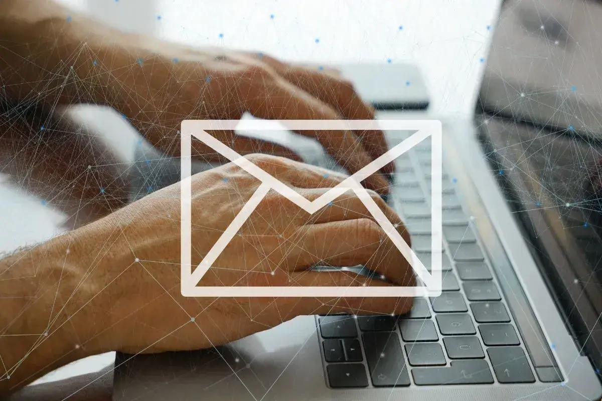Dłonie piszą na klawiaturze laptopa, nad nimi biała ikona koperty i sieć połączeń. Uważaj na spam!